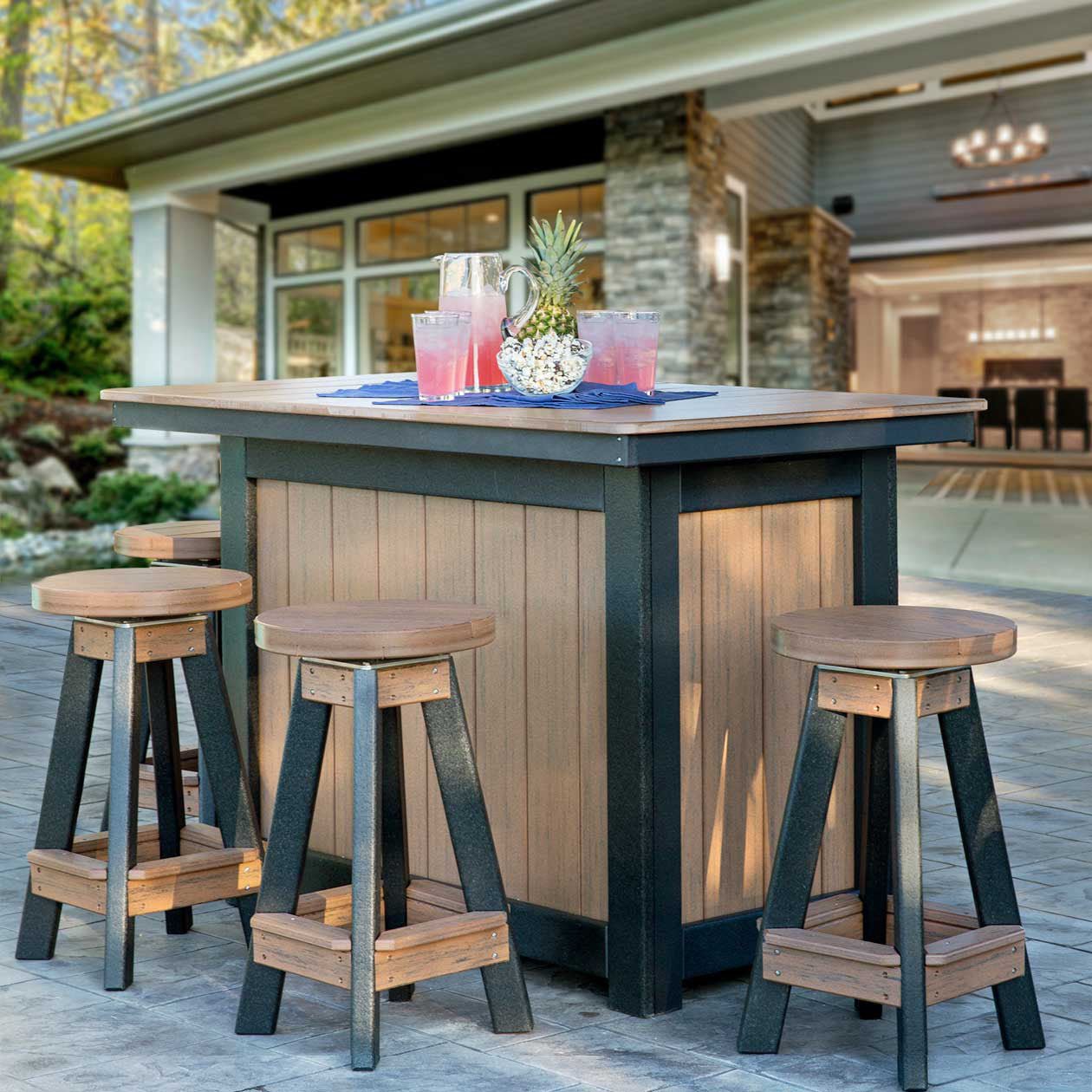 Weathered wood and black poly outdoor bar island with four round swivel bar stools set with lemonade on a stone patio