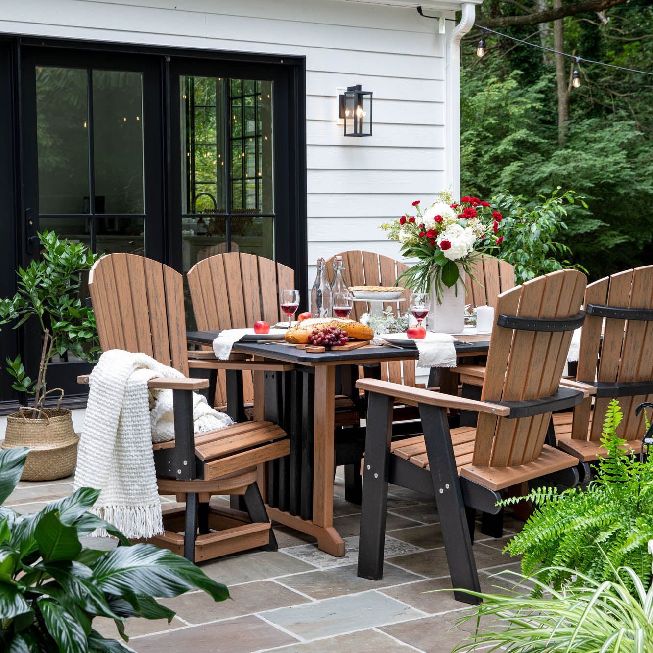 Cedar and black poly 96 inch bistro patio dining table with eight fan back chairs set for dinner on a bluestone patio