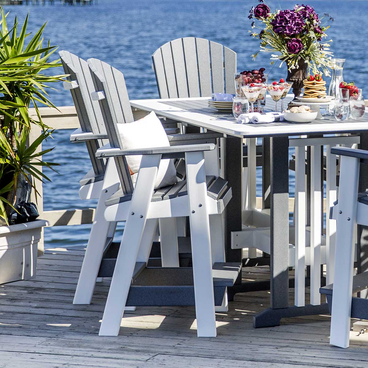 Gray and white poly balcony height Adirondack bar chairs with fan backs pulled up to a table on a lakeside dock
