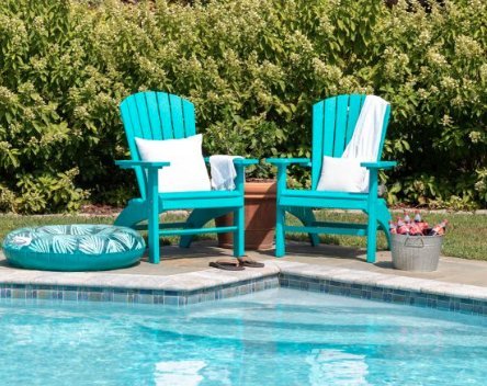 Two aruba blue poly deluxe fanback Adirondack chairs with white pillows and a planter beside a swimming pool