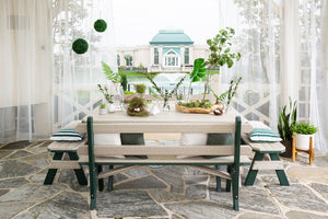 Poly garden table with backed benches and cushions framed by sheer curtains with a fountain view behind