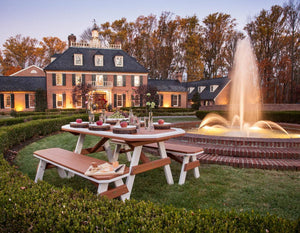 Bordered poly garden table and benches set with apples and flowers on a lawn facing a lit brick estate