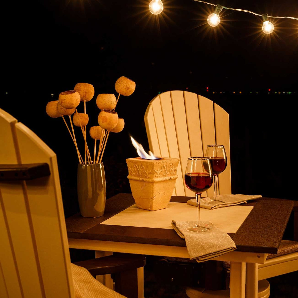 Close up of the square poly bar table at night with wine glasses, napkins and a lit fire pot between chairs
