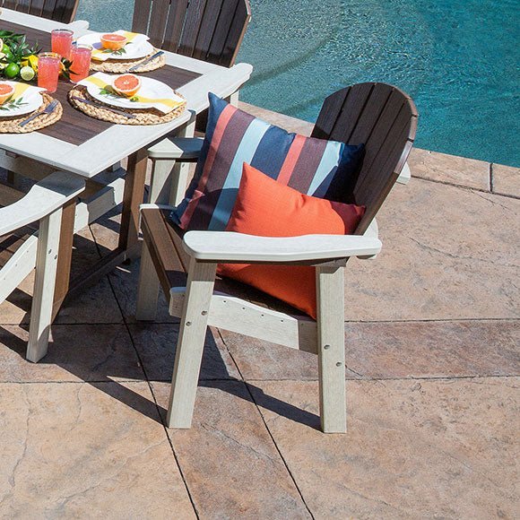 Driftwood poly patio dining arm chair with striped and orange pillows pulled up to a table by the pool
