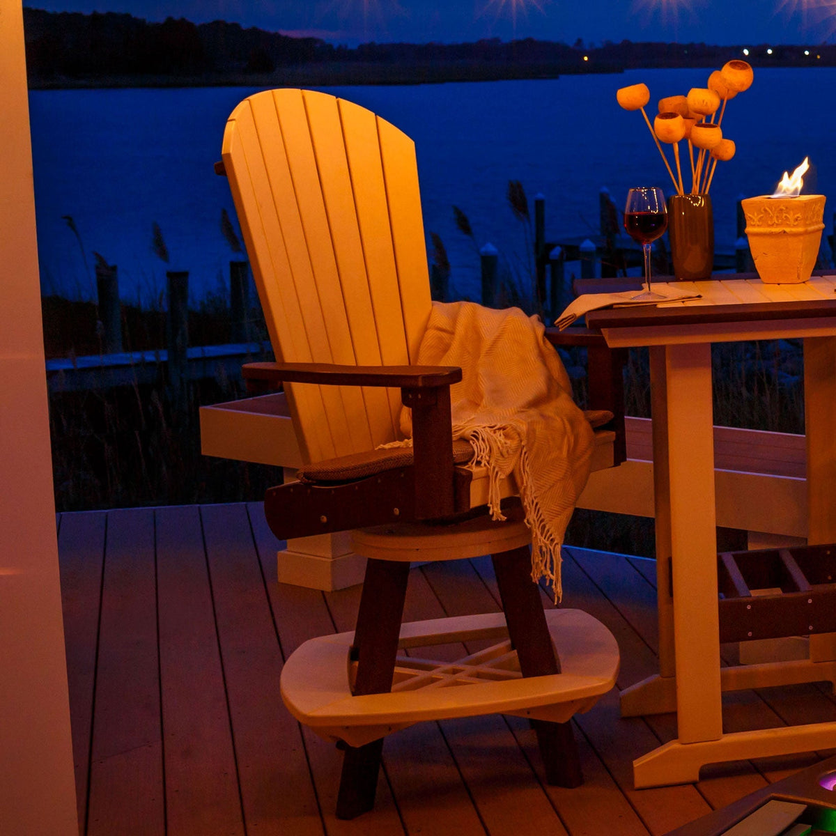 Swivel Adirondack bar chair with a curved footrest ring lit by firelight on a waterfront deck at night