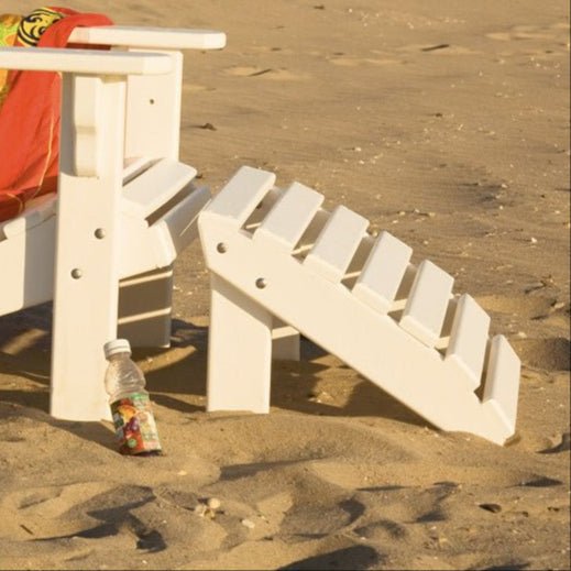 Close-up of a white poly slatted Adirondack ottoman footrest in the sand next to a matching chair