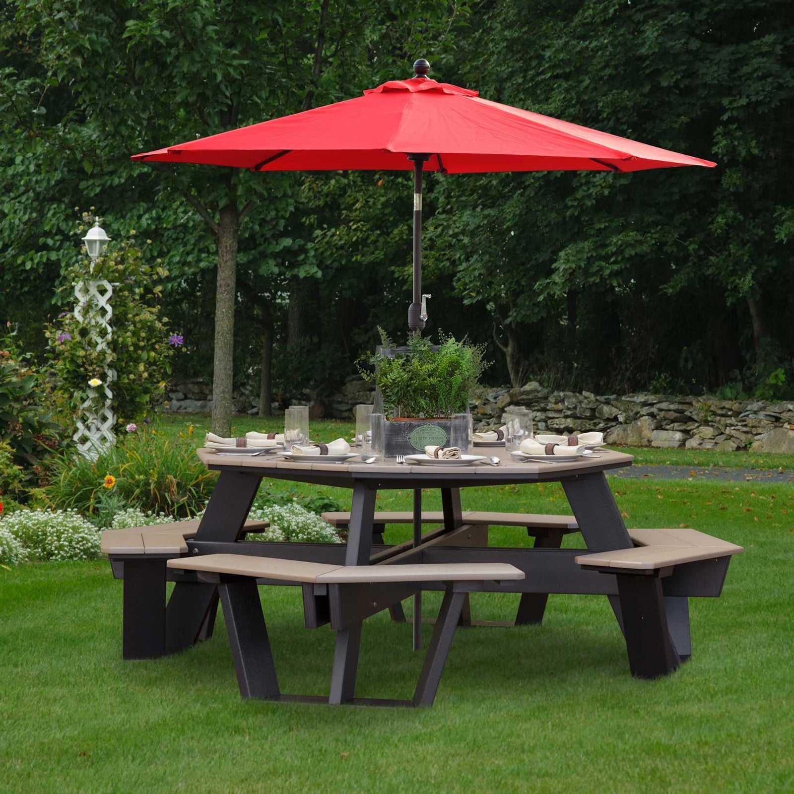 Octagon poly picnic table with tan top, black base and a red umbrella set for dinner on a green lawn