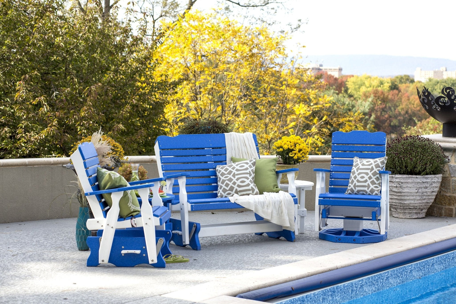 Blue and white poly glider set with a two seat bench glider, two glider chairs and side tables beside a pool