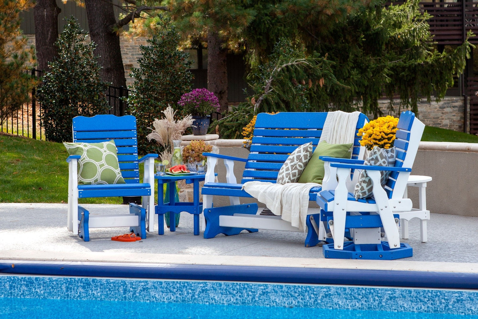 Blue and white poly glider set with a two seat bench glider, two glider chairs and side tables beside a pool
