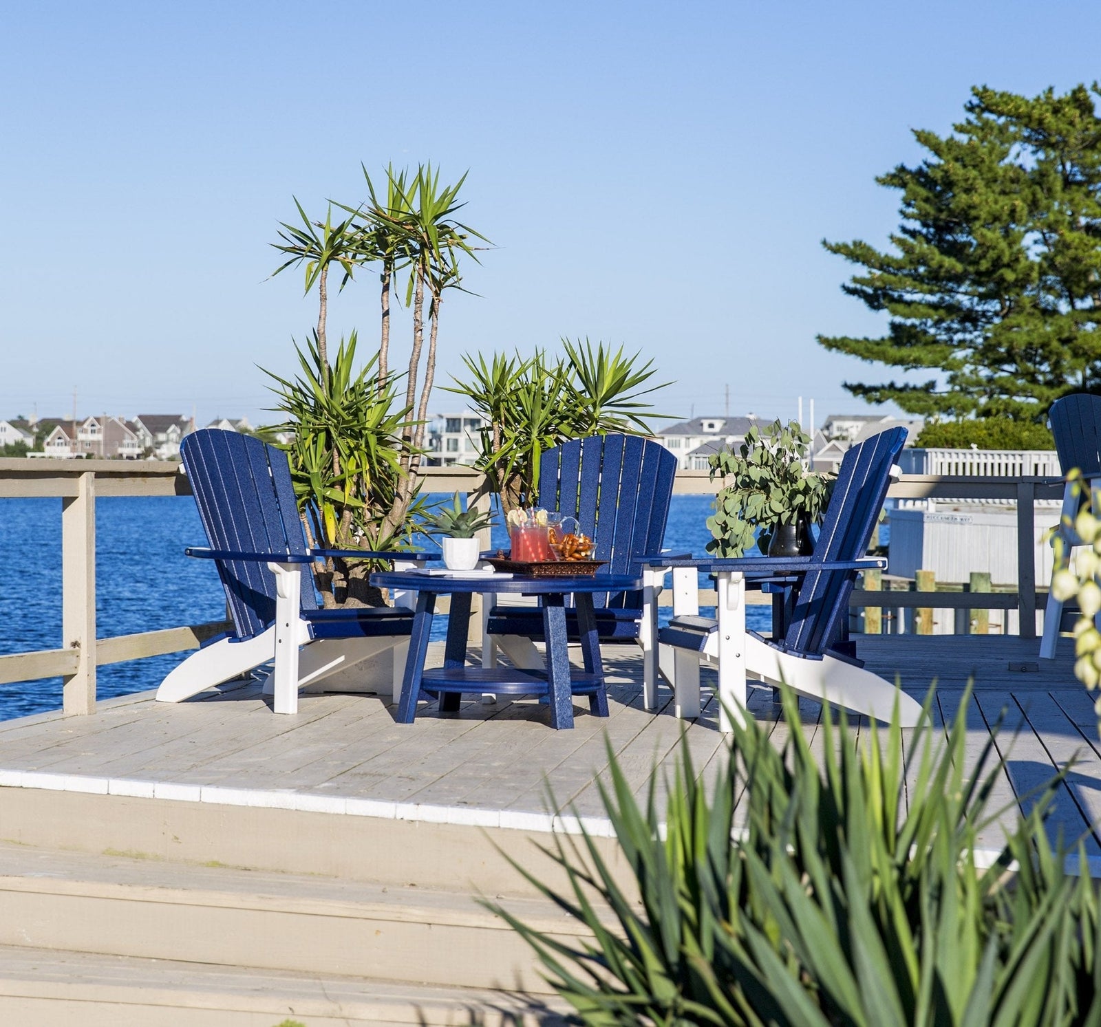 Navy blue and white poly Adirondack chairs around a round poly coffee table on a marina dock at sunset