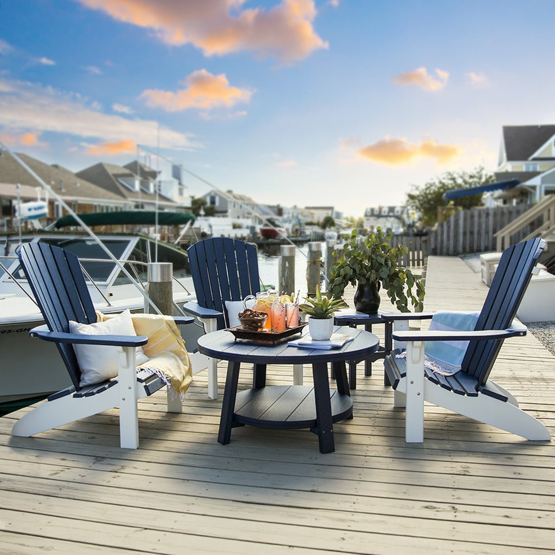 Navy blue and white poly Adirondack chairs around a round poly coffee table on a marina dock at sunset