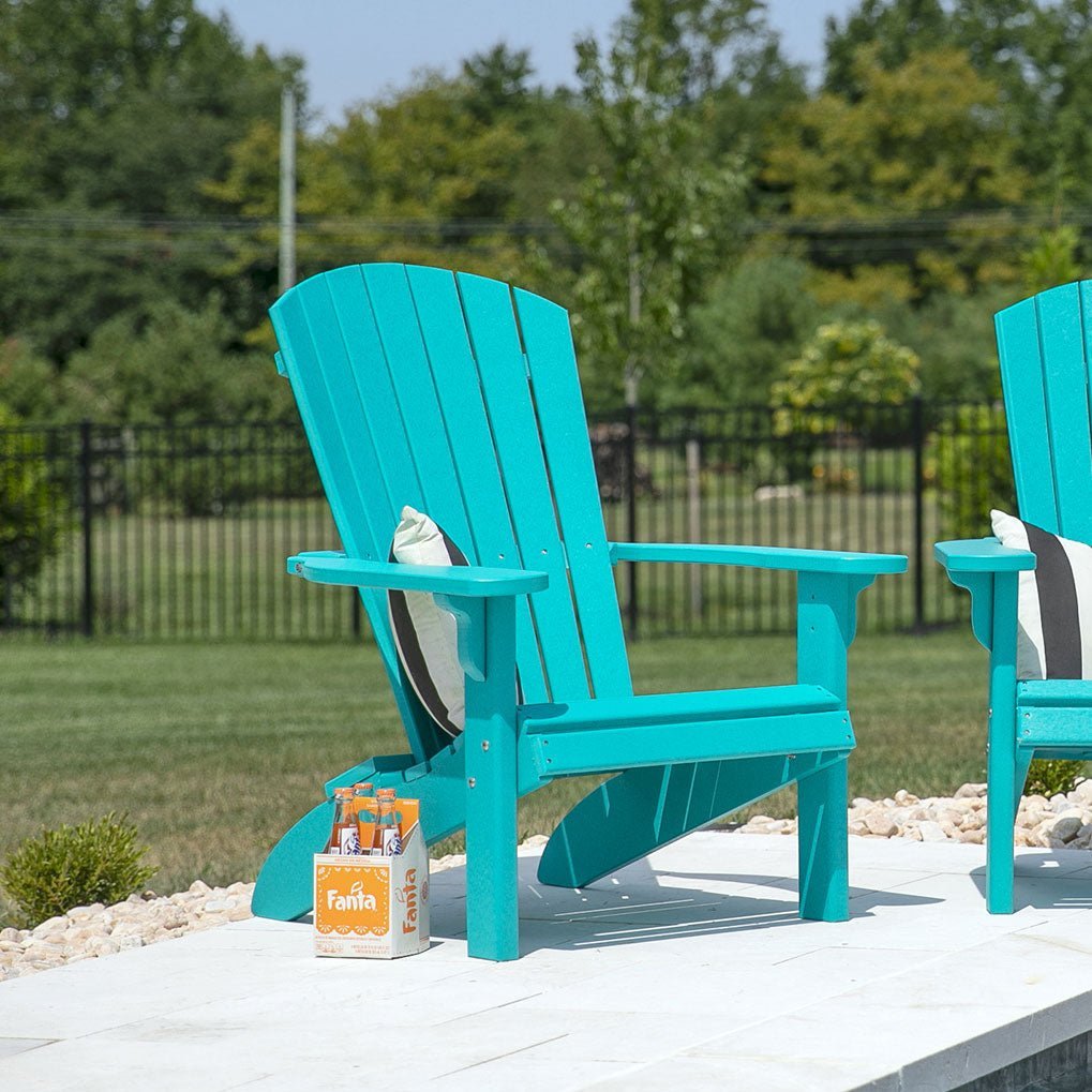 Aruba blue poly Adirondack chairs with striped pillows and soda bottles on a white paver patio in a backyard