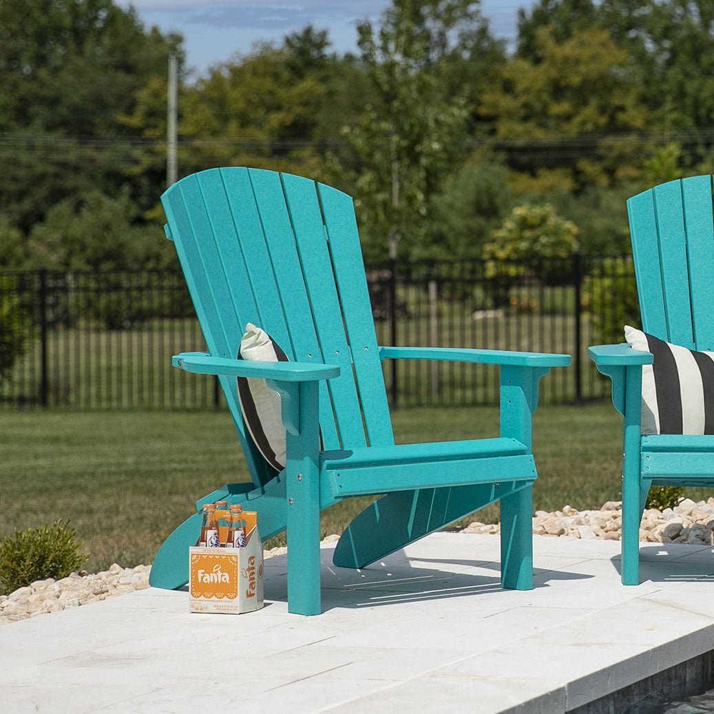 White poly fanback Adirondack chair with a striped beach towel and flip flops on the sand by the ocean