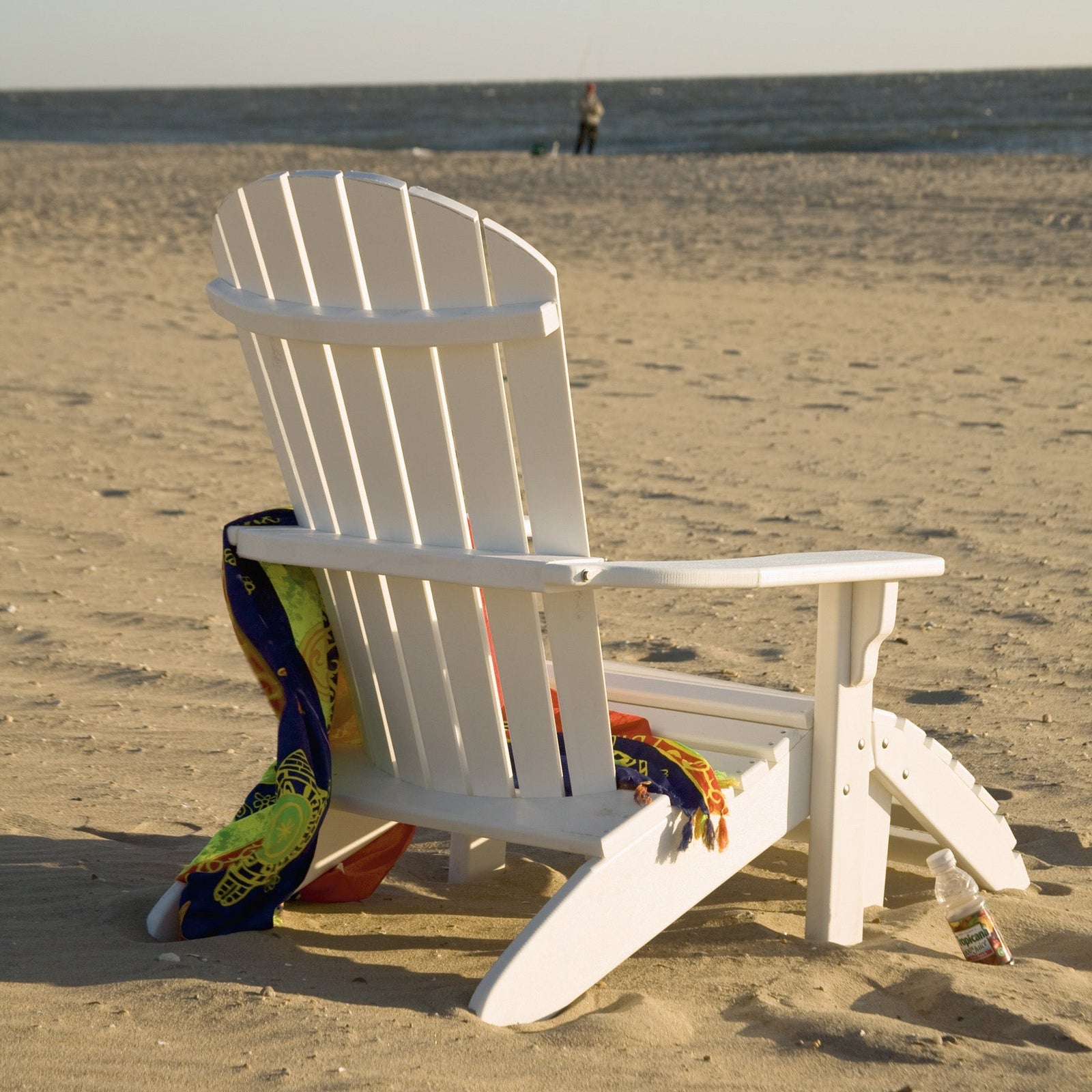 Close-up of a white poly slatted Adirondack ottoman footrest in the sand next to a matching chair