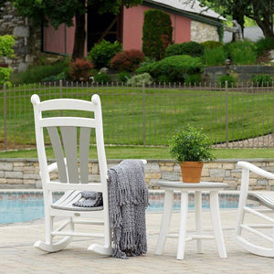 White poly rocking chair with a gray throw beside a round side table with a potted plant near a pool