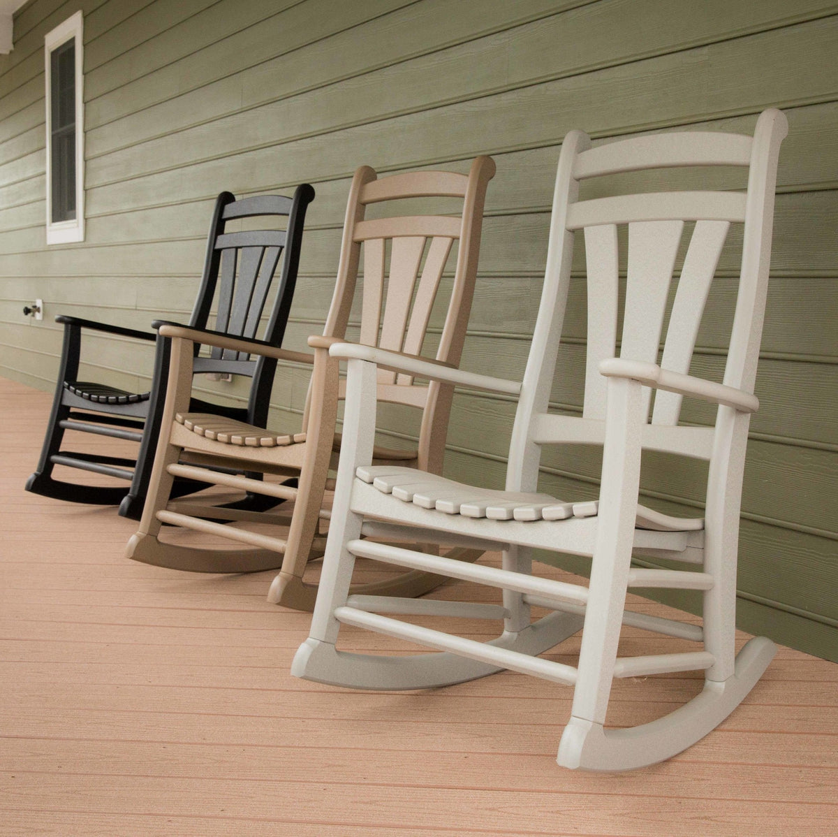Four poly rocking chairs in black, weatherwood, tan and white lined up along a porch with green siding