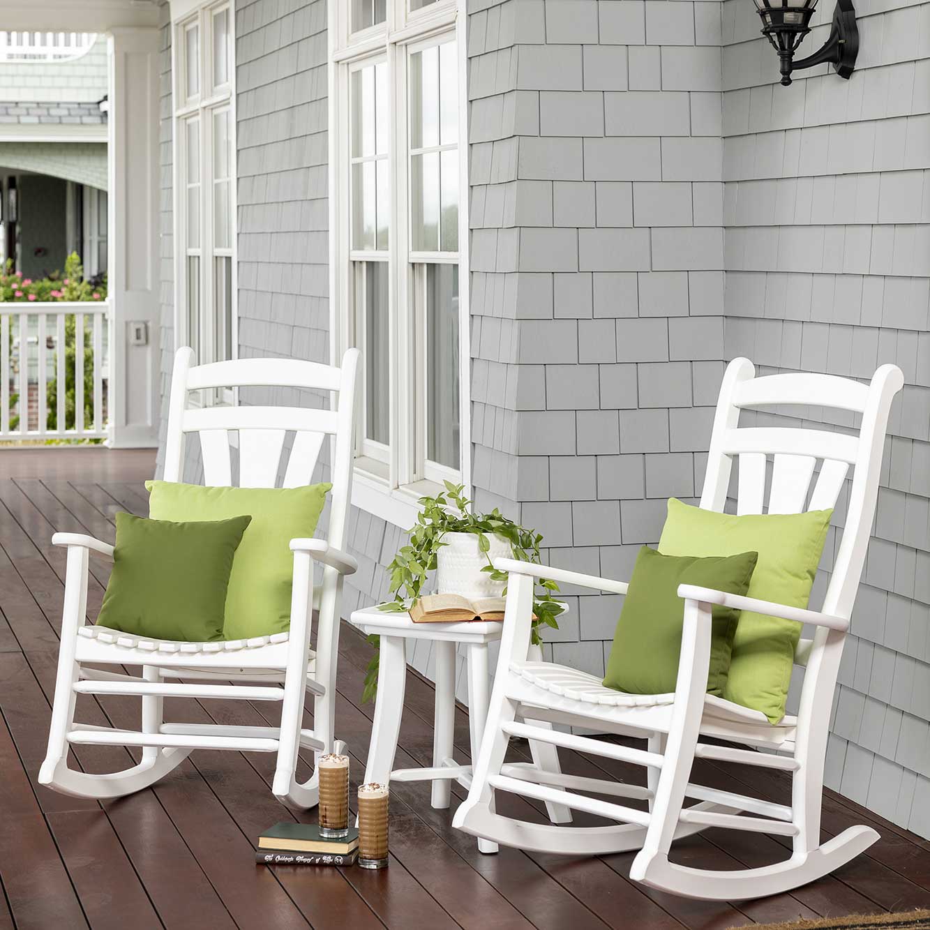 Two white poly rocking chairs with fanned back slats and a round side table on a paver patio by a pool