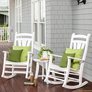 Two white poly rockers with green pillows and a small side table with books on a shingled porch