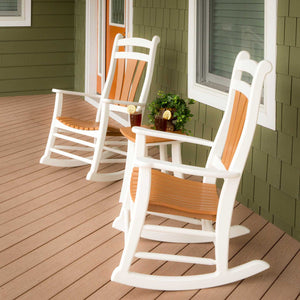Two white and cedar poly rocking chairs facing each other with iced tea on a side table on a porch