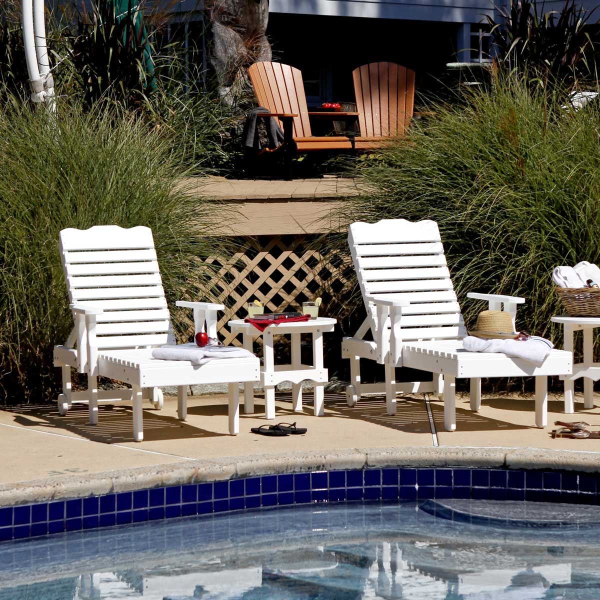 Two white poly chaise sun loungers with adjustable slat backs and a scalloped side table set on a pool deck