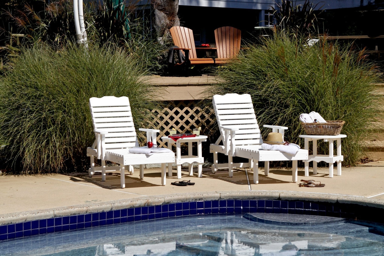 Two white poly chaise sun loungers with adjustable slat backs and a scalloped side table set on a pool deck