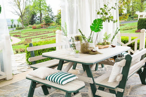 Driftwood and green poly garden table with two backed benches and pillows on a curtained stone patio