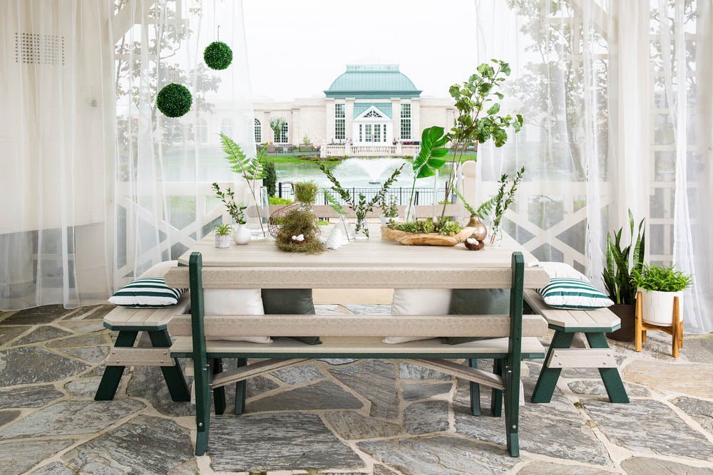 Poly garden table with backed benches and cushions framed by sheer curtains with a fountain view behind
