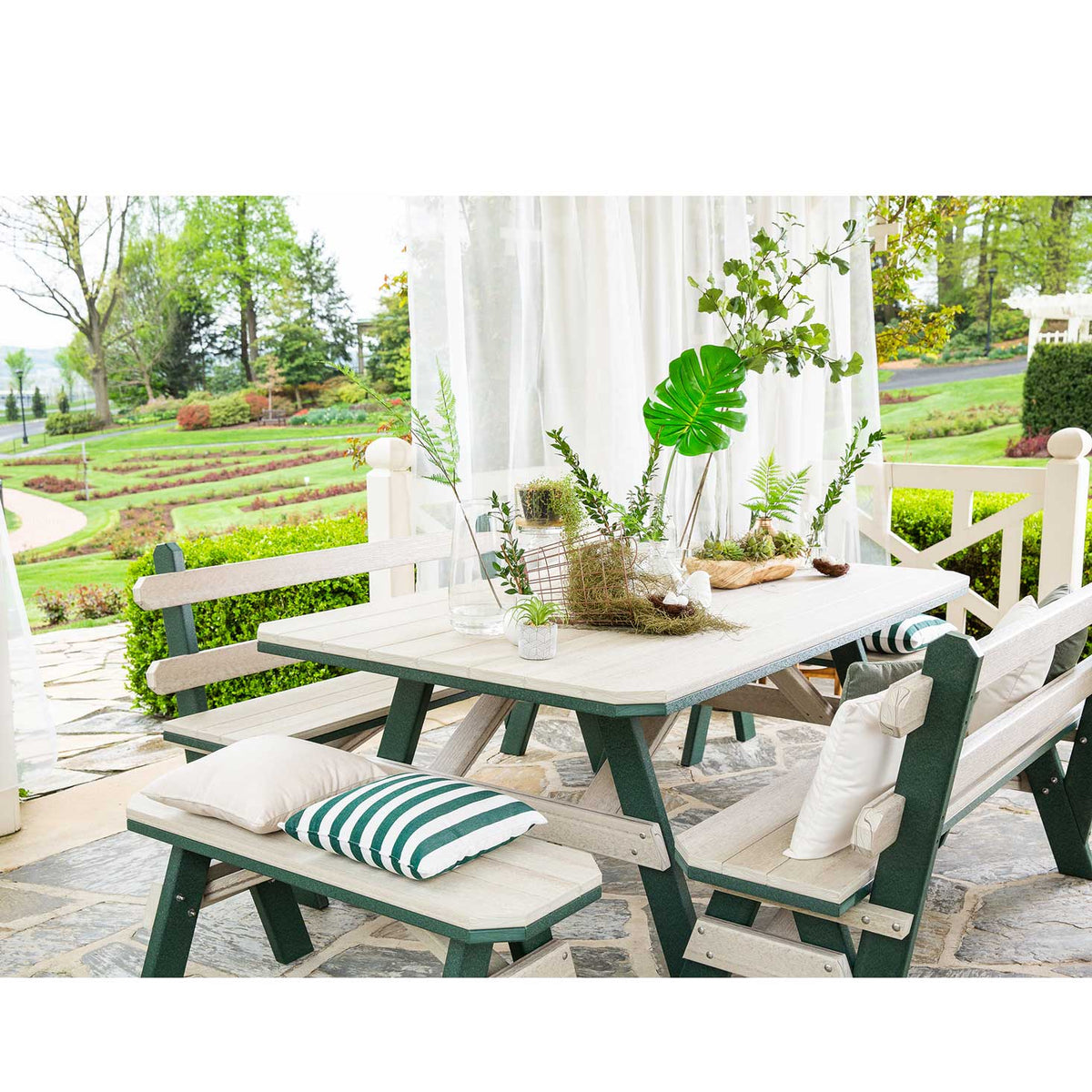 Driftwood and green poly garden table with a backed bench and two backless benches with striped pillows on flagstone