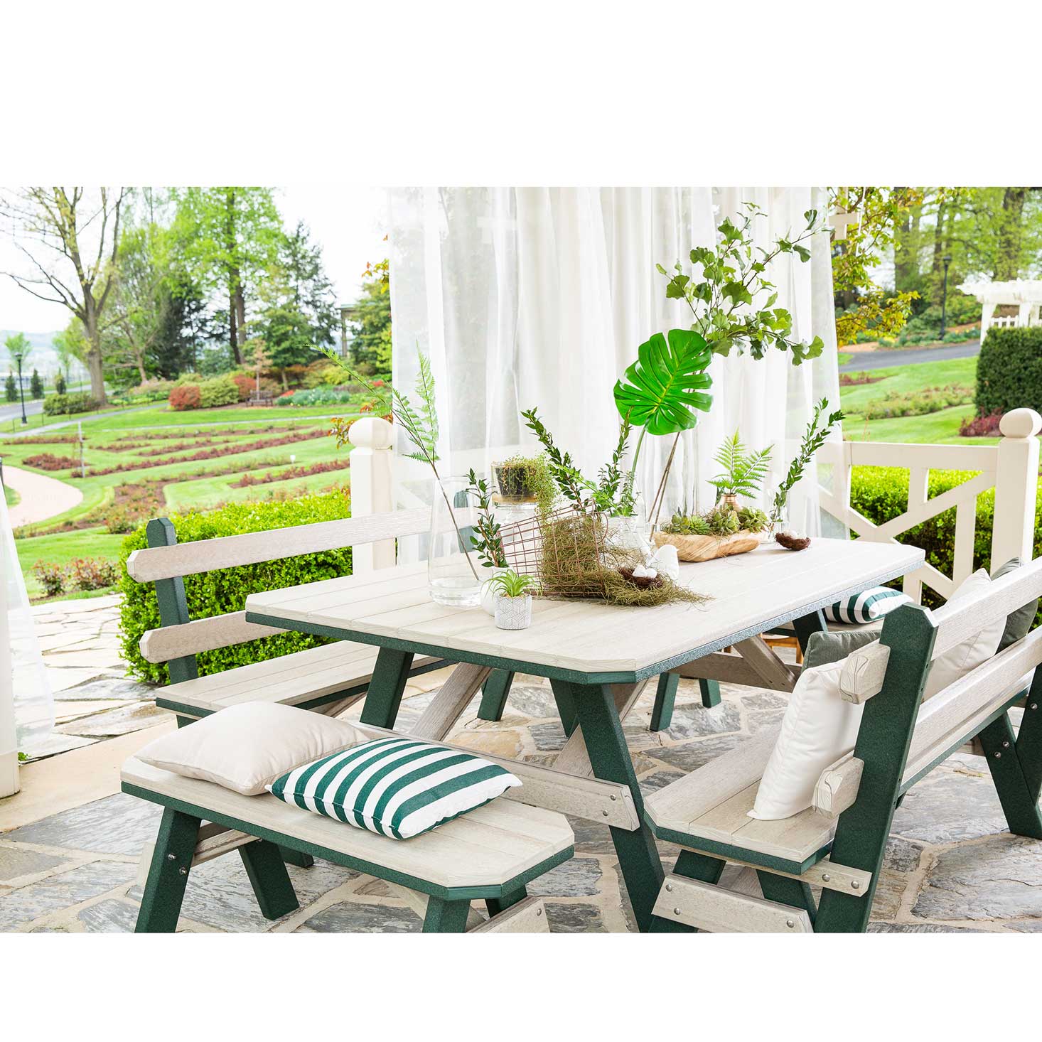 Driftwood and green poly garden table with a backed bench and two backless benches with striped pillows on flagstone