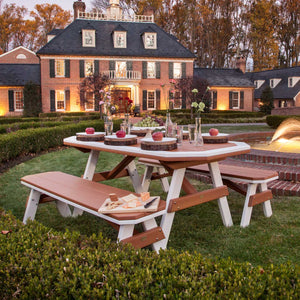 Cedar and white poly garden table with four benches set with apples and cheese on a lawn before a brick estate
