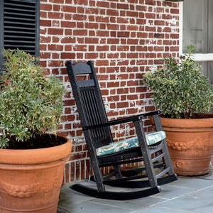 Black poly porch rocking chair with tall slat back between terracotta planters against a red brick wall