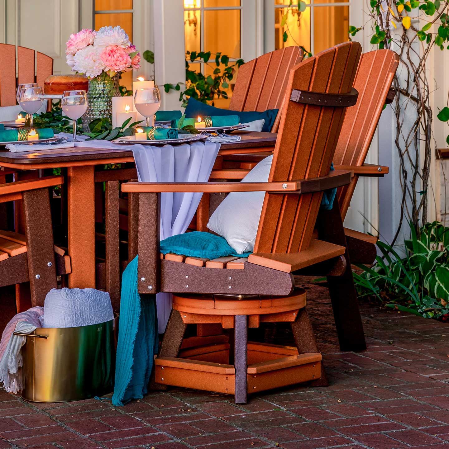 Cedar and brown poly swivel bistro chairs at a candlelit outdoor dining table with pillows and draped linens