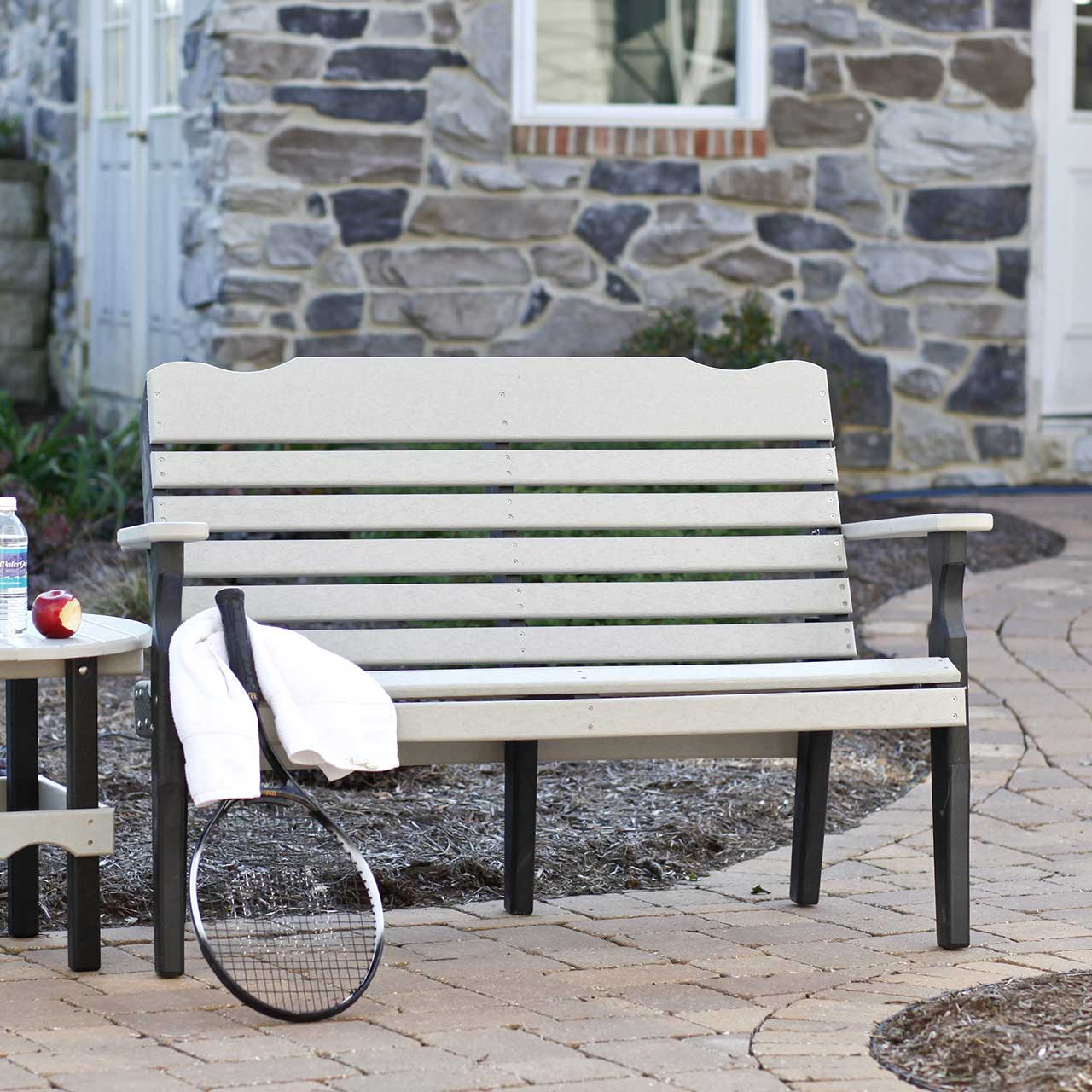 Weatherwood and black poly West Chester 4 foot patio bench with curved slat back and arms on a paver patio