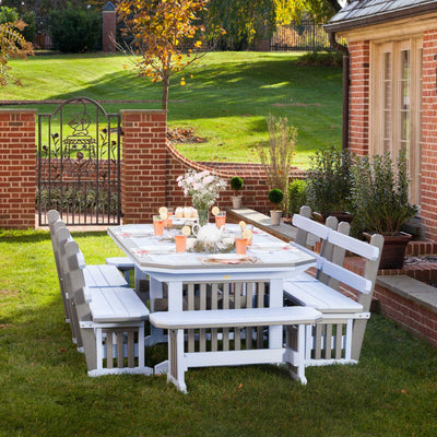 White and weatherwood Mission poly table with four benches set for a party on a lawn by a brick garden gate