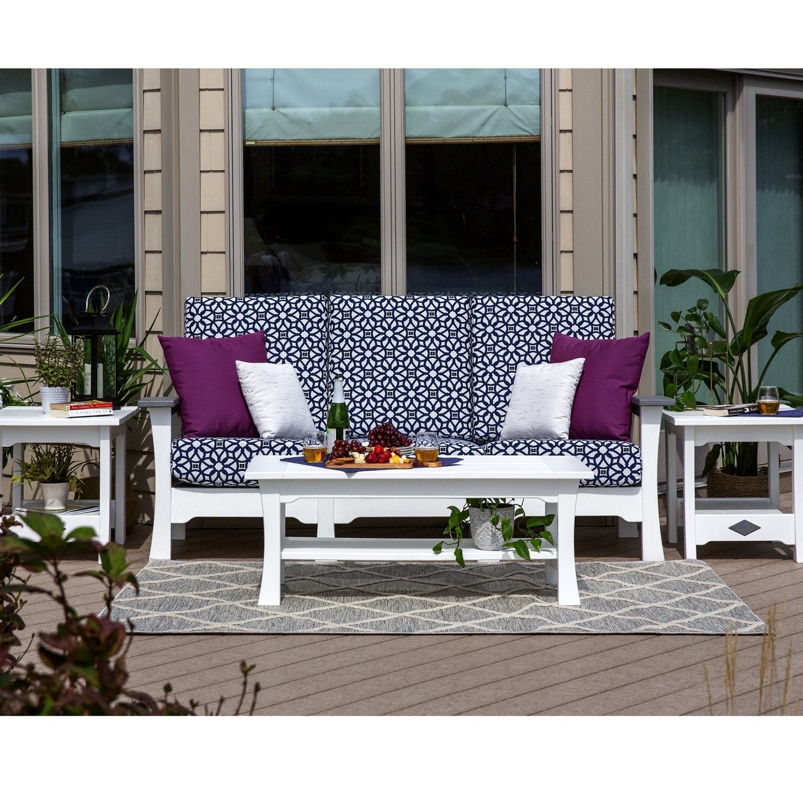 White poly outdoor sofa with navy patterned cushions and purple pillows, flanked by end tables and a coffee table