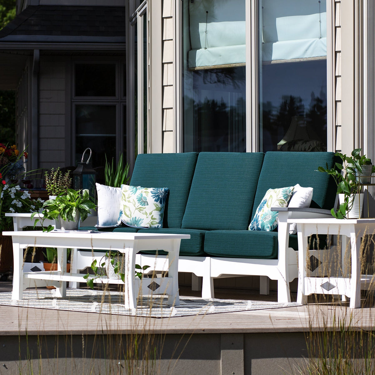 White poly deep seating sofa with teal cushions and floral pillows, coffee table and side tables on a porch