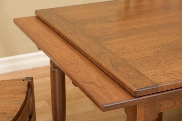 Close-up of the draw leaf pulling out from beneath the cherry table top above a turned leg