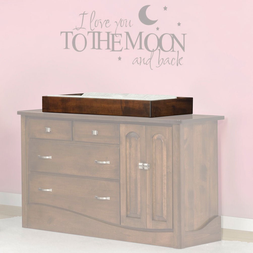 Walnut changing tray set on top of a gray dresser in a pink nursery with a moon wall decal