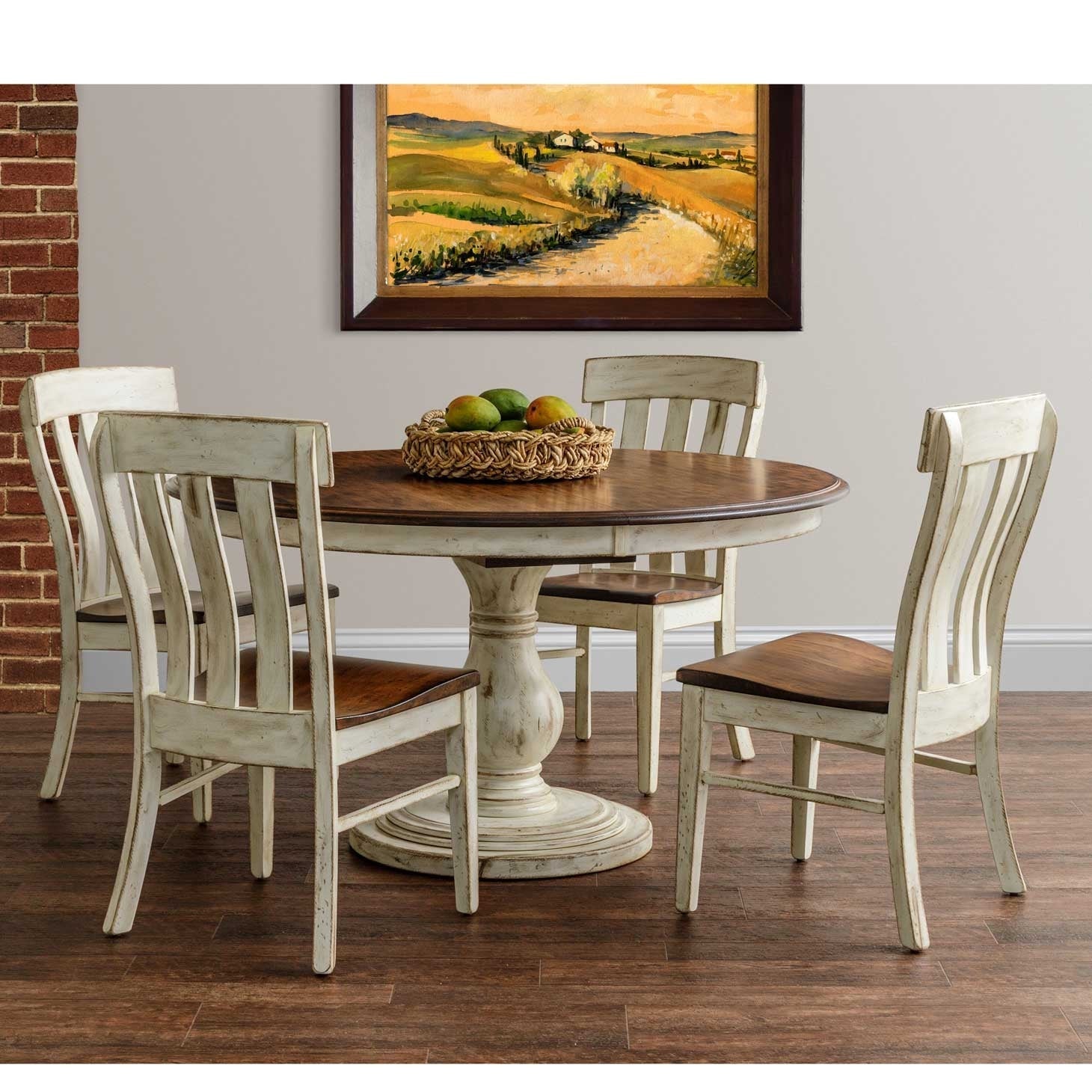 Two-tone round pedestal table with four white slat-back chairs, a fruit basket and Tuscan landscape art