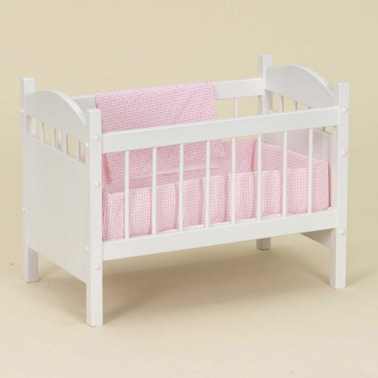 White wooden doll crib with arched head and foot panels, spindle rails and pink polka dot bedding with a bumper