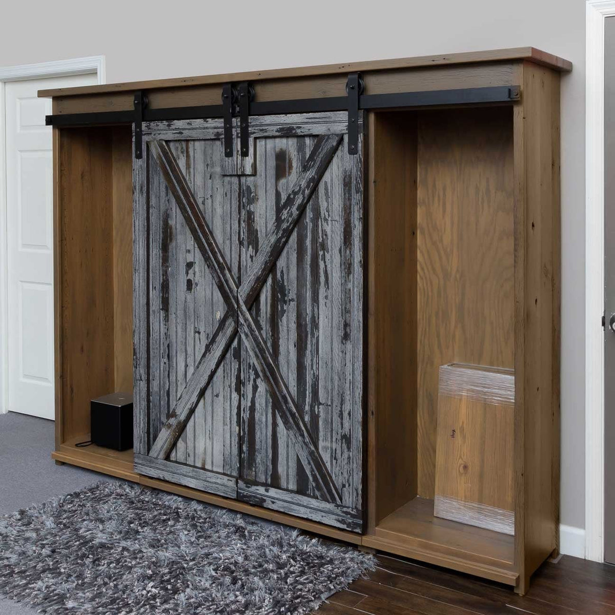 Angled view of a rustic barnwood TV wall unit, both weathered barn doors slid to the center over the open shelving and lower storage bay