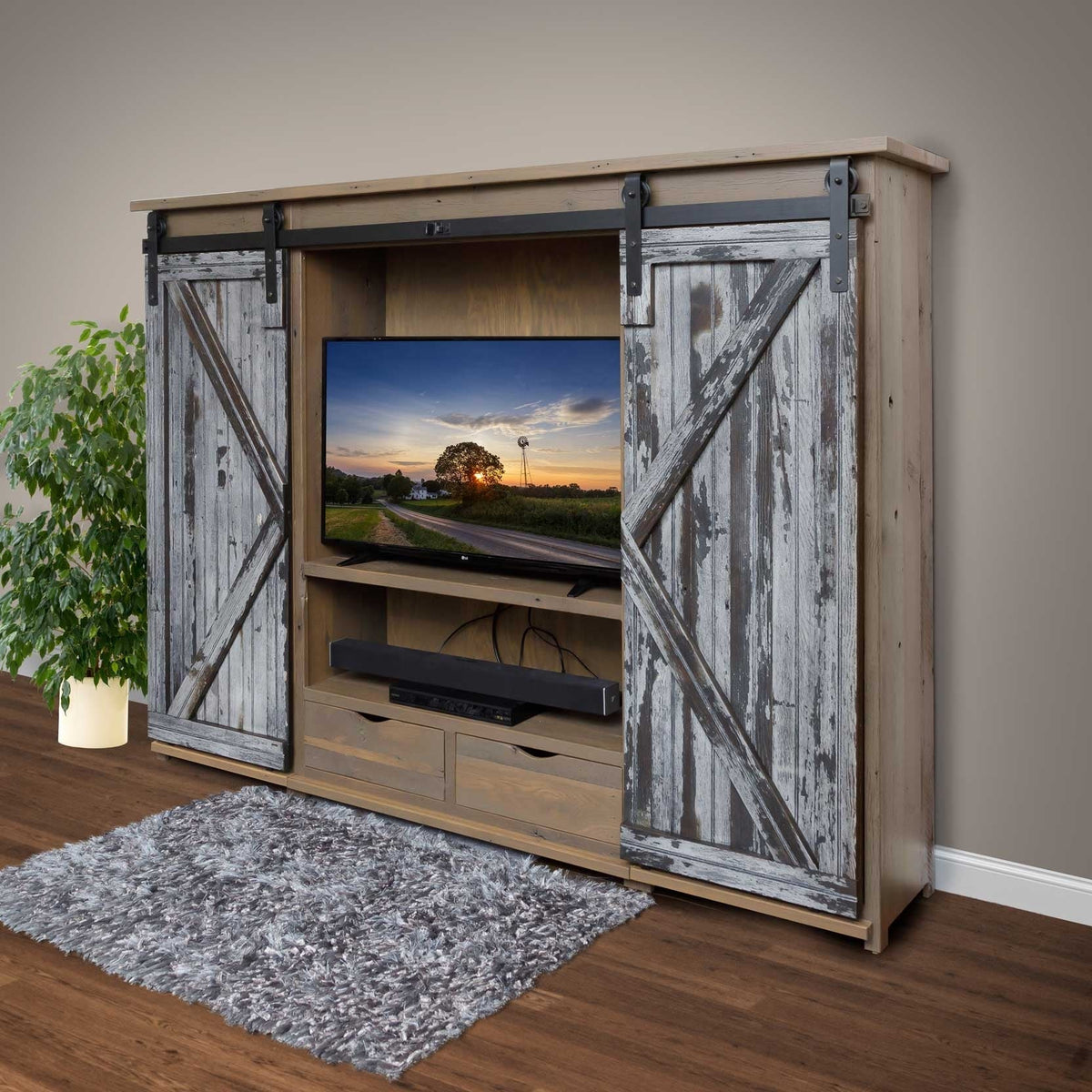 Reclaimed barnwood entertainment wall unit with weathered gray sliding barn doors on black rails, open TV bay, sound bar shelf and two drawers