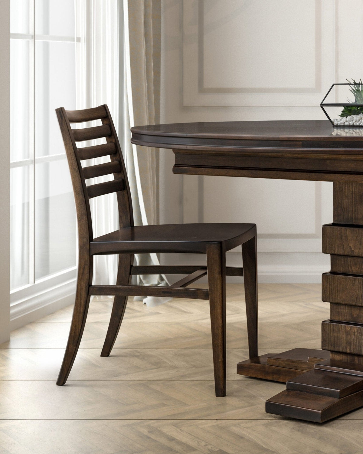Dark walnut ladder back side chair beside a round pedestal dining table in a bright paneled room