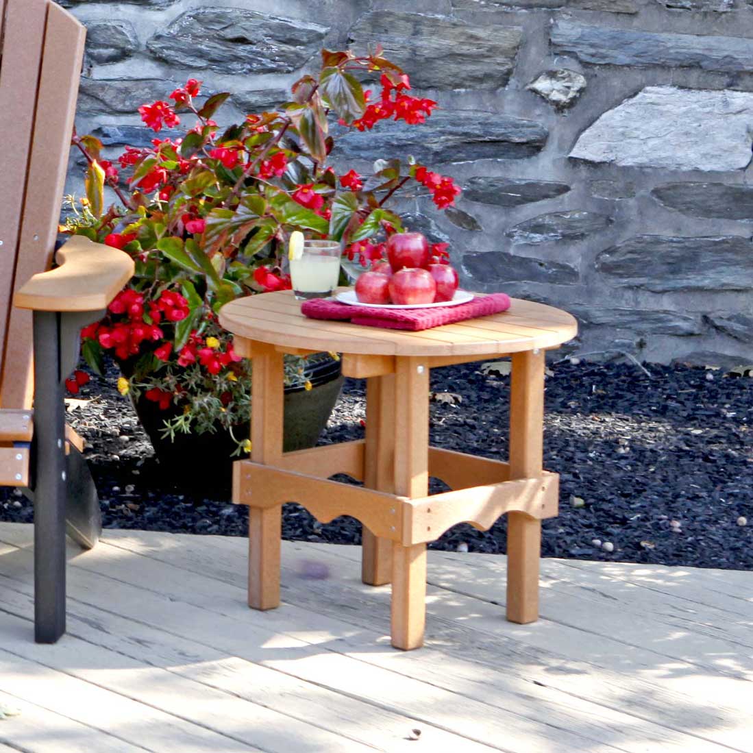 Cedar poly round patio side table on a deck holding lemonade and apples next to a chair and red begonias