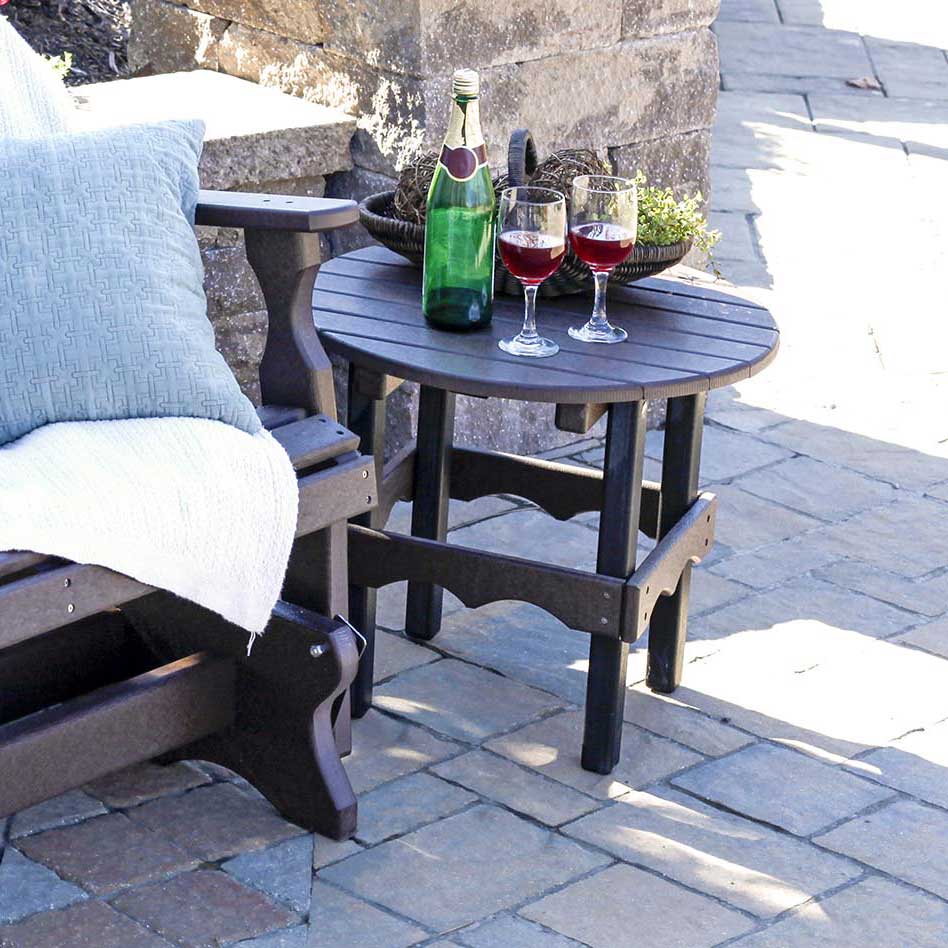 Dark brown and black poly round side table holding wine glasses and a bottle beside a cushioned glider on pavers