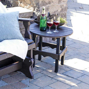 Dark brown and black poly round side table holding wine glasses and a bottle beside a cushioned glider on pavers