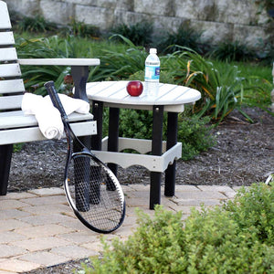 Two tone gray and black round poly patio side table on pavers next to a bench, with towels and a tennis racket