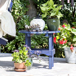 Navy blue poly round patio side table holding potted plants and a lidded jar beside a porch swing