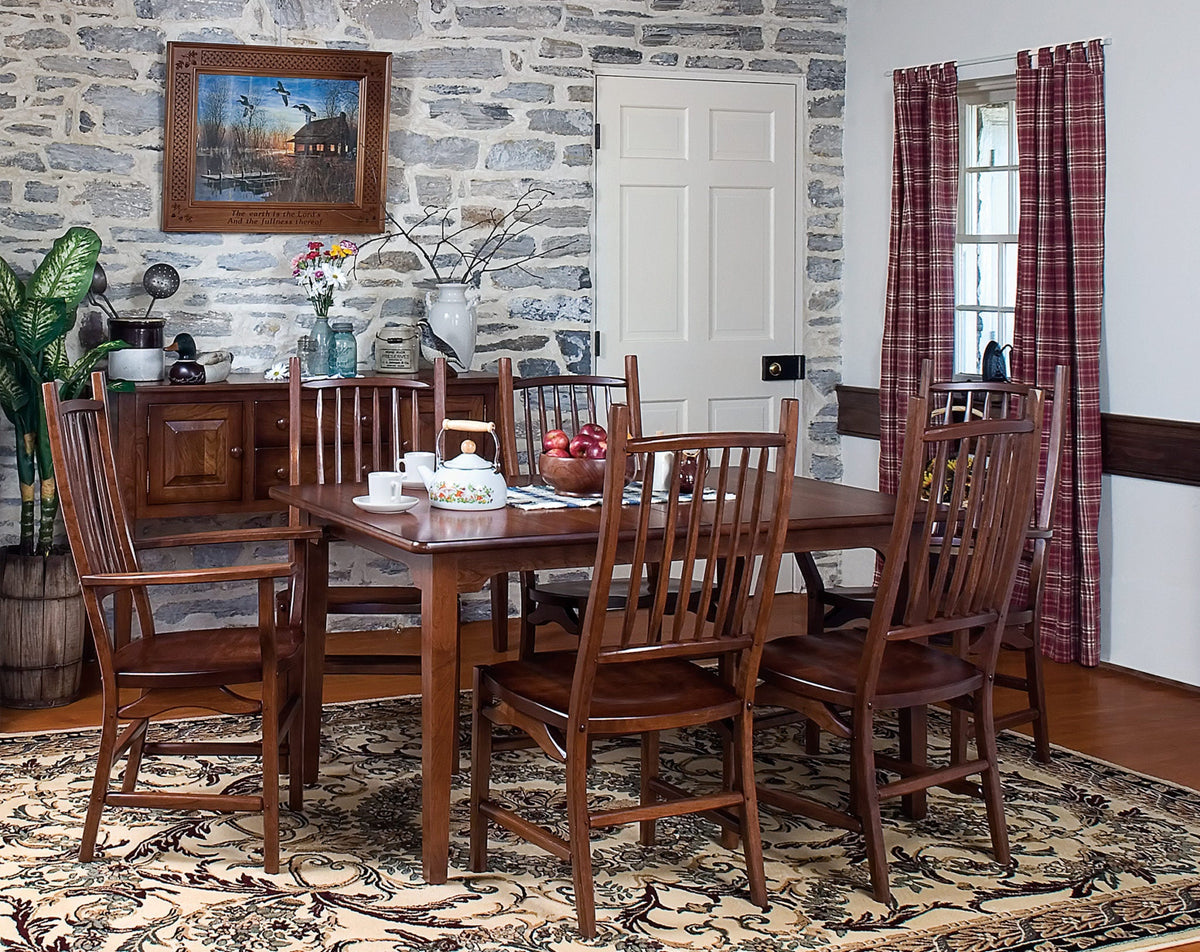 Cherry dining table with six tall slat back chairs in a stone walled farmhouse dining room