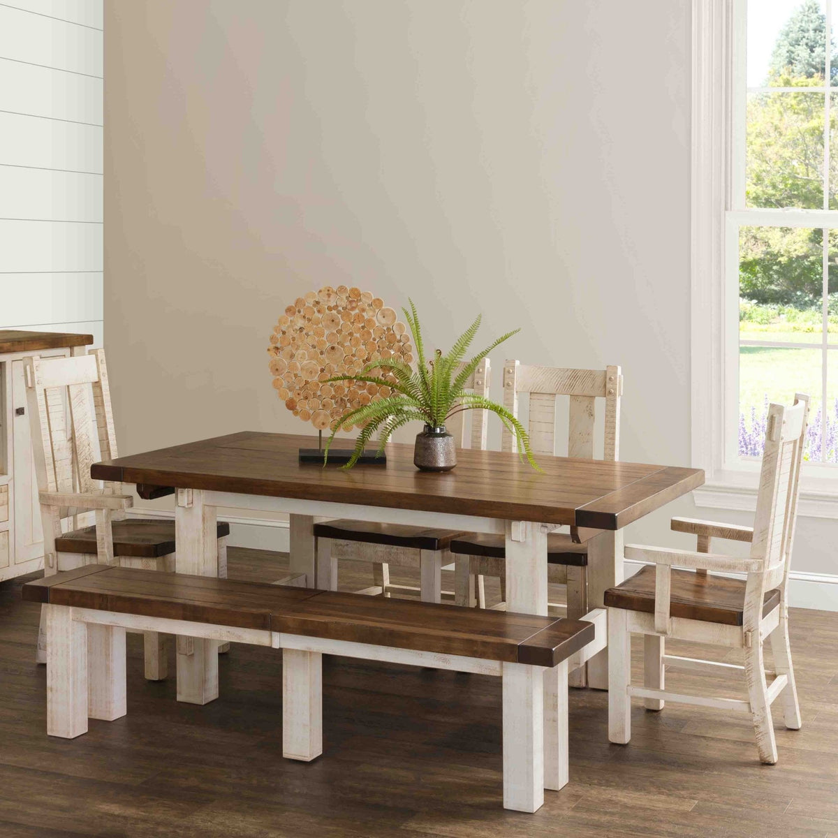 Farmhouse dining set with a distressed white base, dark plank tabletop, matching bench and rustic chairs in a bright dining room